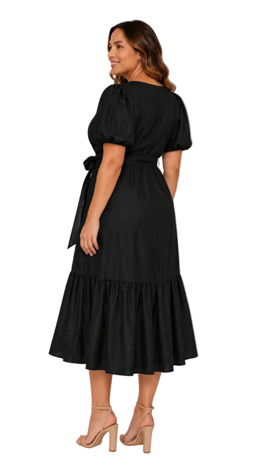A woman modeling a black faux midi dress with puff sleeves, a tie waist, and a tiered ruffle hem, shown from the back against a light gray studio background.