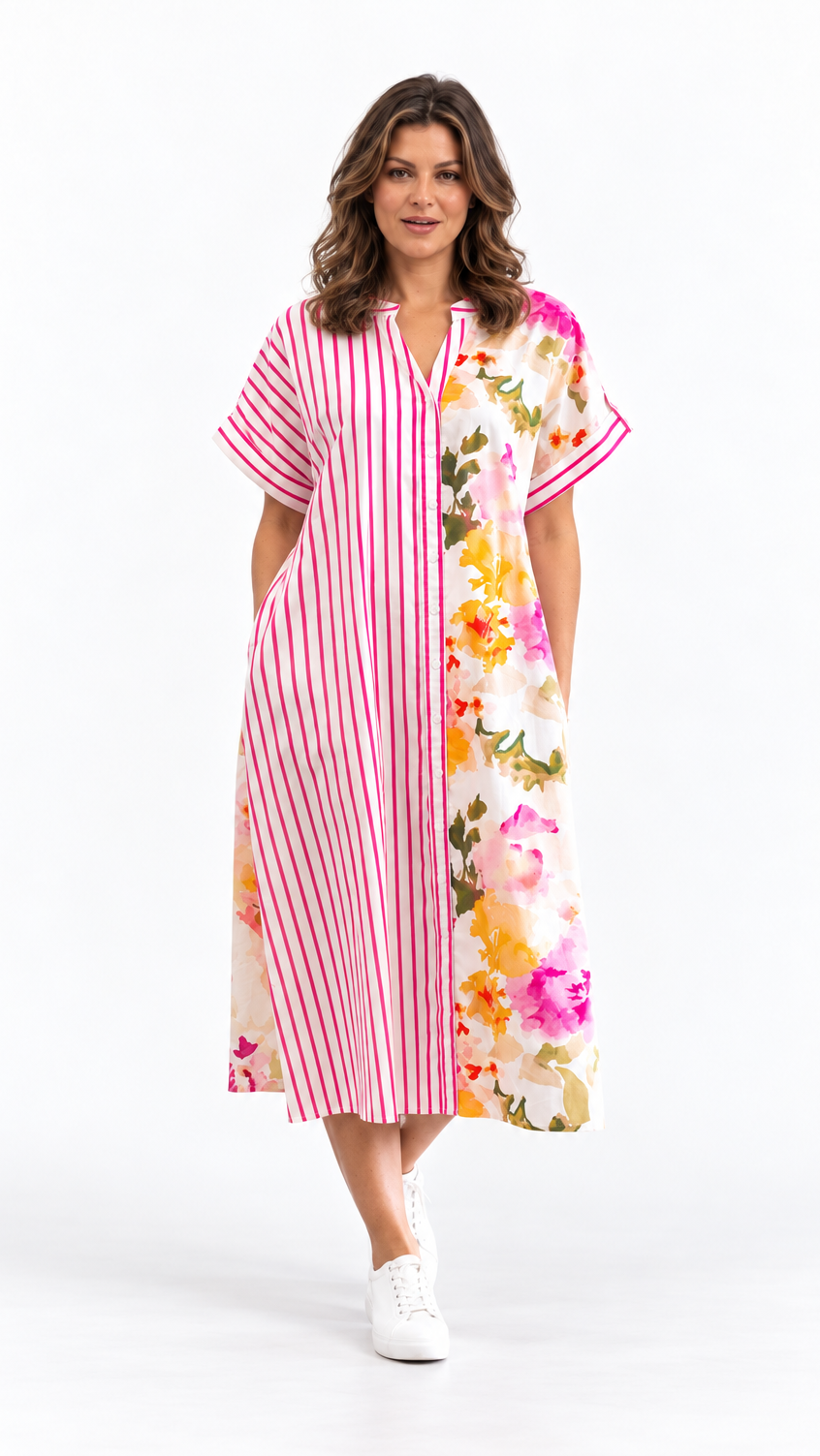 A woman modeling a short-sleeve midi dress with a split design: one side features vertical pink and white stripes, and the other side has a colorful floral print. She is wearing white sneakers against a plain white studio background.