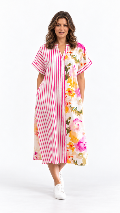 A woman modeling a short-sleeve midi dress with a split design: one side features vertical pink and white stripes, and the other side has a colorful floral print. She is wearing white sneakers against a plain white studio background.