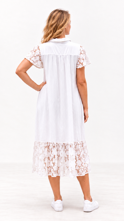 A woman viewed from the back wearing a white midi dress with short lace sleeves and a lace hem, paired with white sneakers, against a clean white studio background.