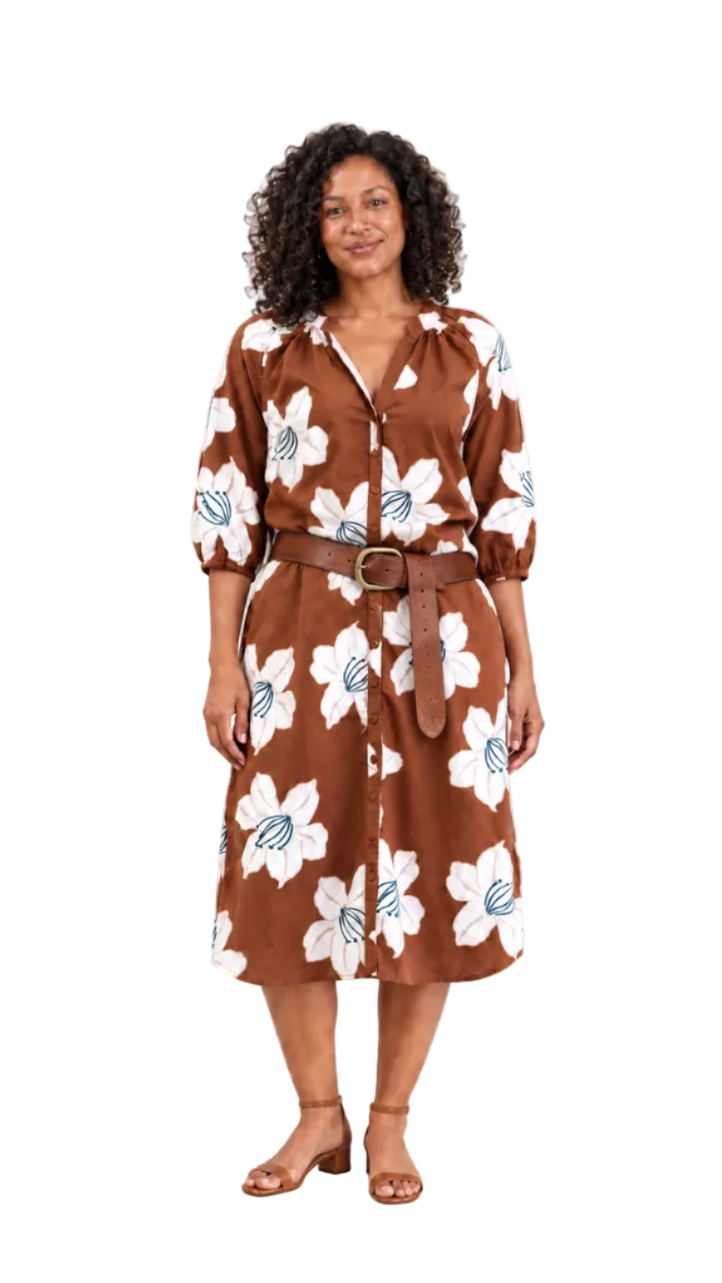 A woman modeling a brown midi shirt dress with a white floral pattern, blue leaf accents, and a matching brown belt with a gold buckle, set against a plain light background.