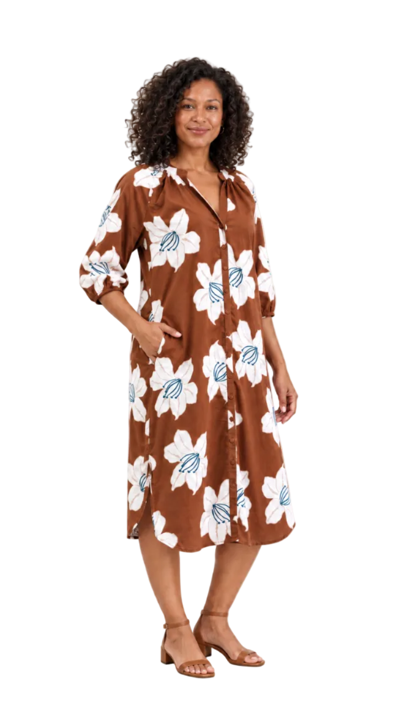 A woman modeling a brown midi dress with a white and light blue floral print, standing against a plain off-white studio background.