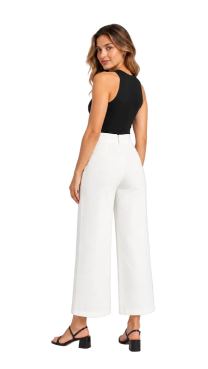 A woman modeling white wide-leg cropped pants with a black sleeveless top and black block-heel sandals, photographed against a light gray studio background.