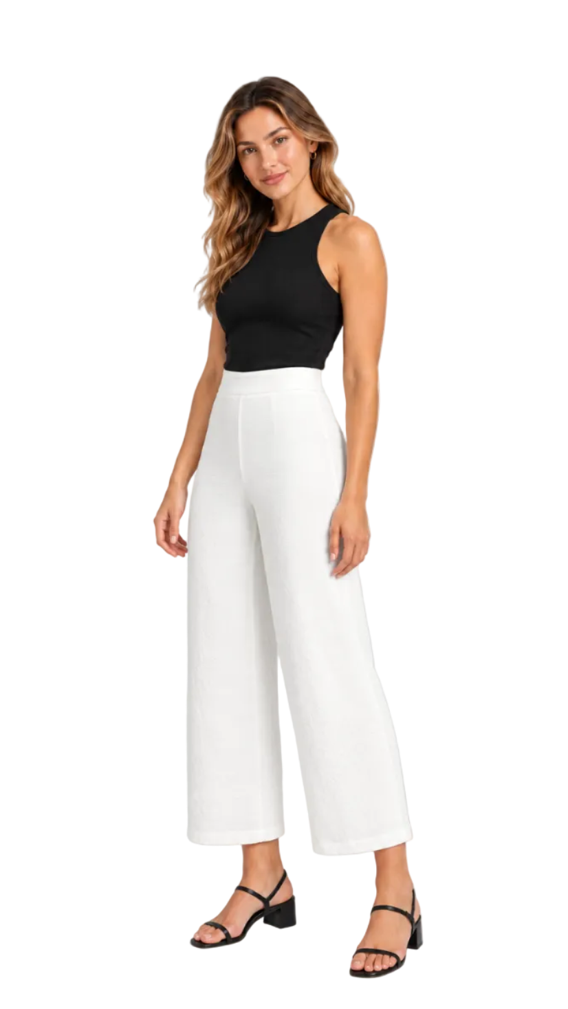 A woman modeling a black sleeveless crop top and white wide-leg cropped pants with black strappy sandals, photographed against a light gray studio background.