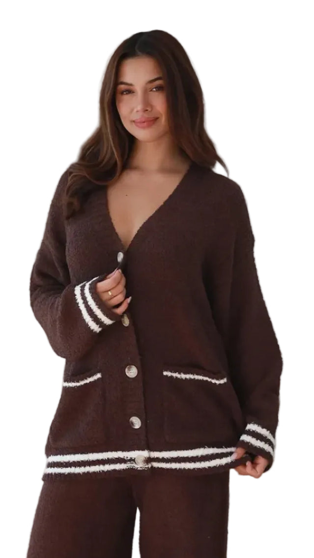 A woman modeling a dark brown knit cardigan and matching pants set. The cardigan features white striped trim on the cuffs, hem, and pocket edges, with white buttons down the front.