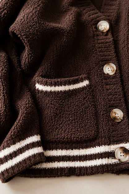 Close-up of a dark brown textured knit cardigan with white stripe details on the pocket and hem, and brown buttons.