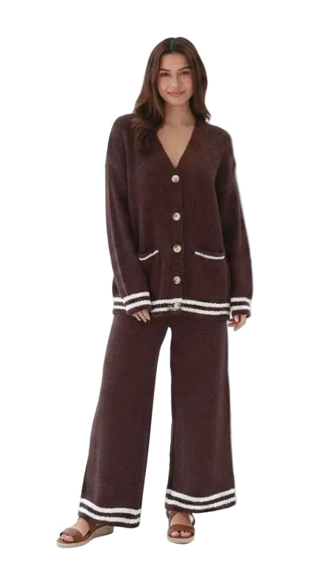 A woman modeling a matching knit lounge set consisting of a dark brown button-front cardigan and wide-leg pants, both featuring white striped trim at the cuffs and hems, set against a plain white background.