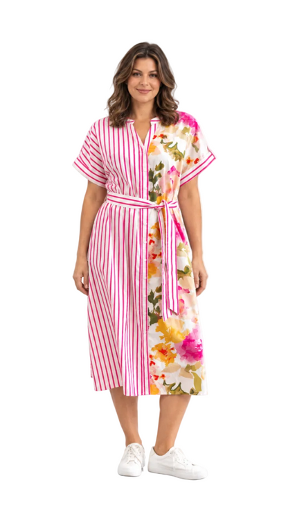 A woman modeling a short-sleeve midi dress with a split design: one side features pink and white vertical stripes, and the other side features a colorful floral print with pink, yellow, orange, and green flowers on a white background. She is wearing white sneakers against a plain white studio background.