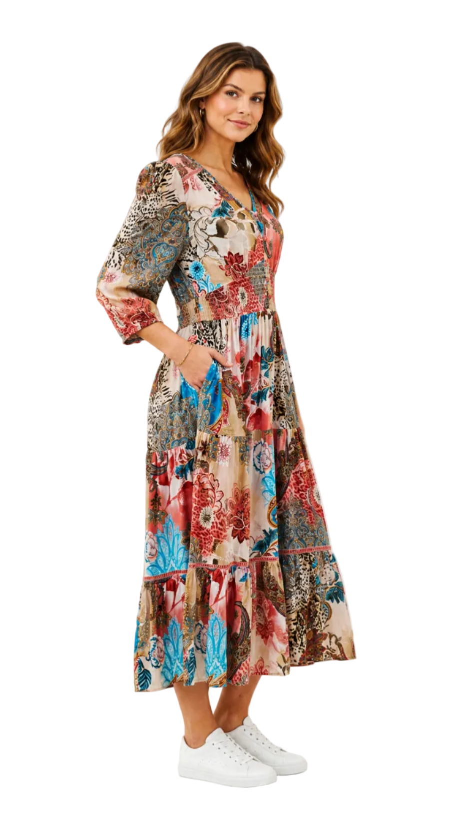 A woman modeling a long-sleeve midi dress with a colorful floral and paisley print, paired with white sneakers, against a plain white background.