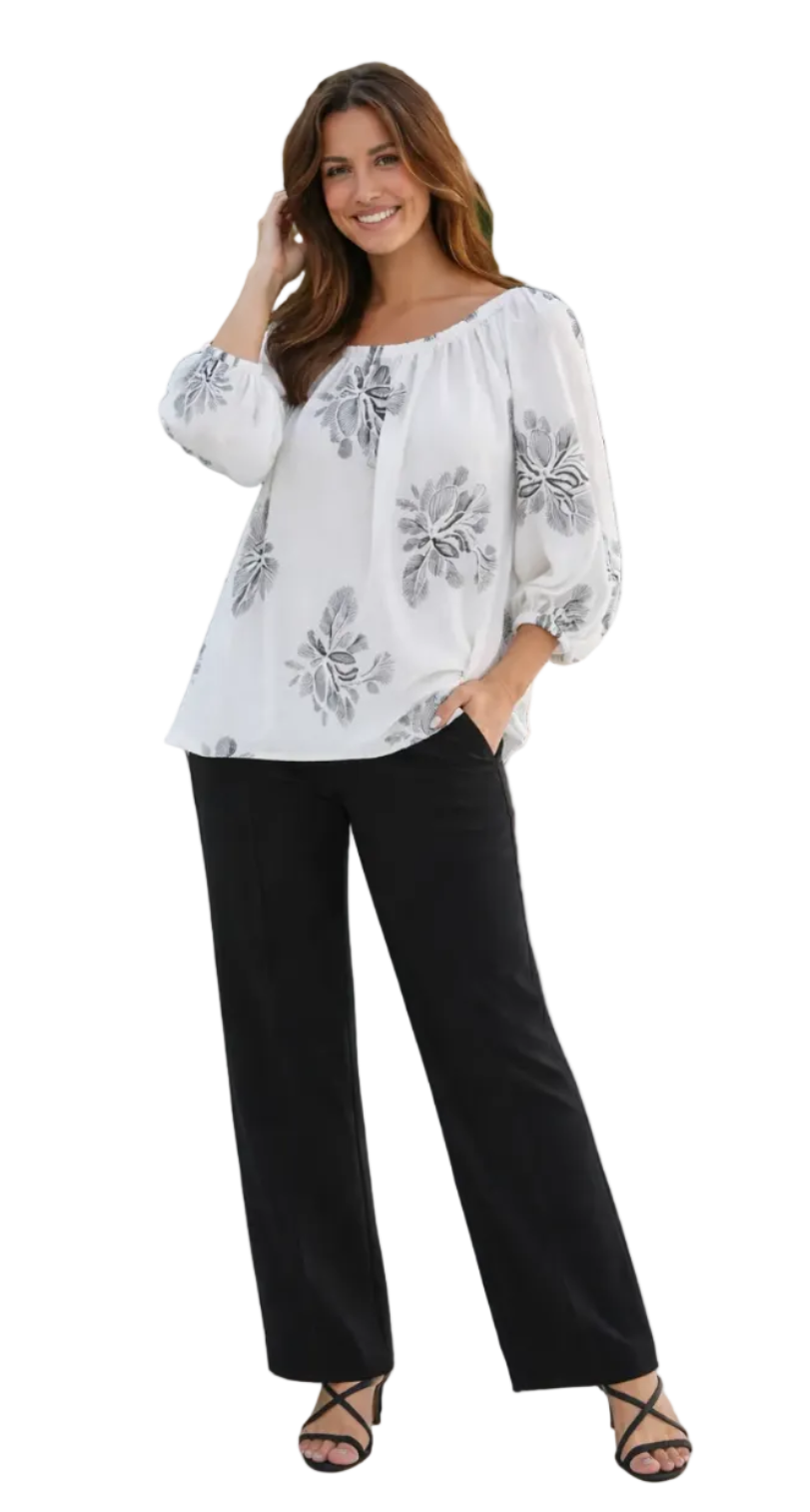 Woman wearing a white blouse with black floral patterns and black pants on a white background