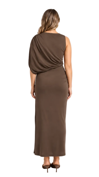 A woman viewed from the back wearing a sleeveless, floor-length draped dress in a warm brown shade, paired with brown pointed-toe heels, against a clean white studio background.