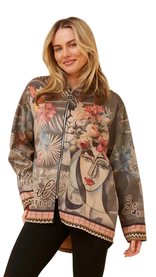 A woman wearing a brown zip-up bomber jacket with a colorful graphic print of a face, flowers, and botanical elements, paired with black pants, against a plain white background.
