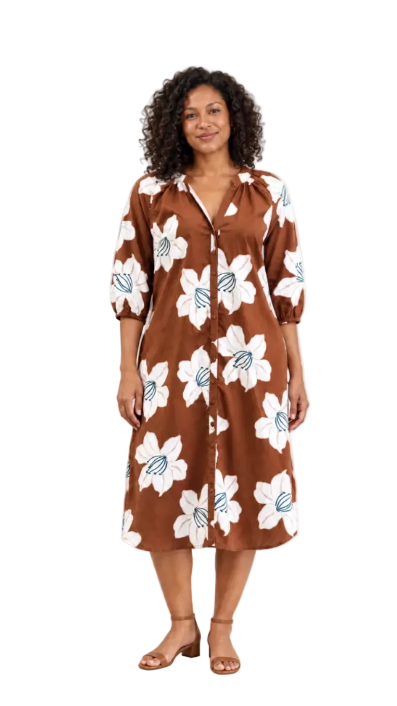 A woman modeling a brown midi shirt dress with a white floral print and blue accents, standing against a plain off-white studio background.