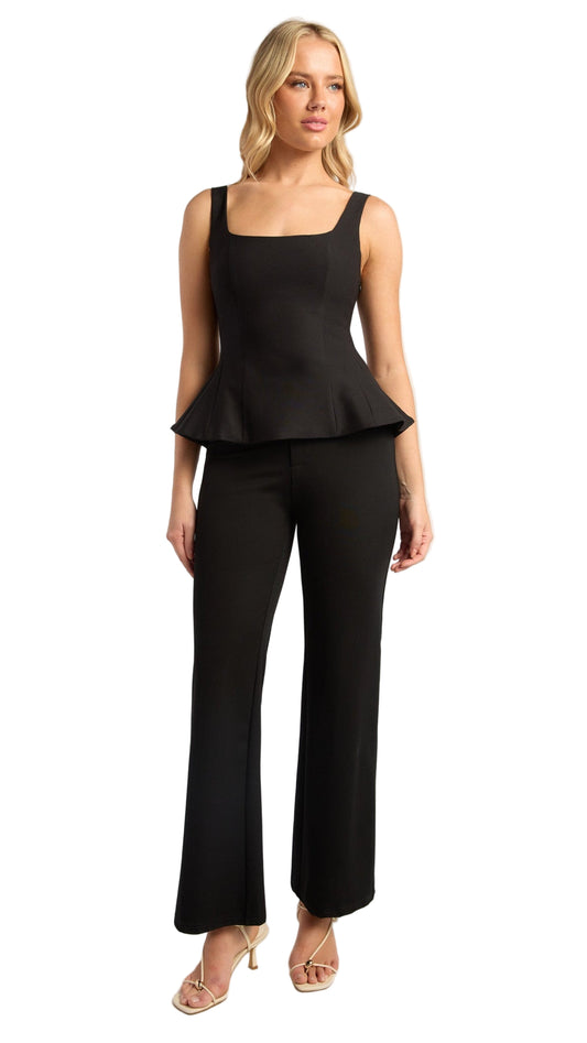 Woman wearing a black peplum top and black pants on a white background