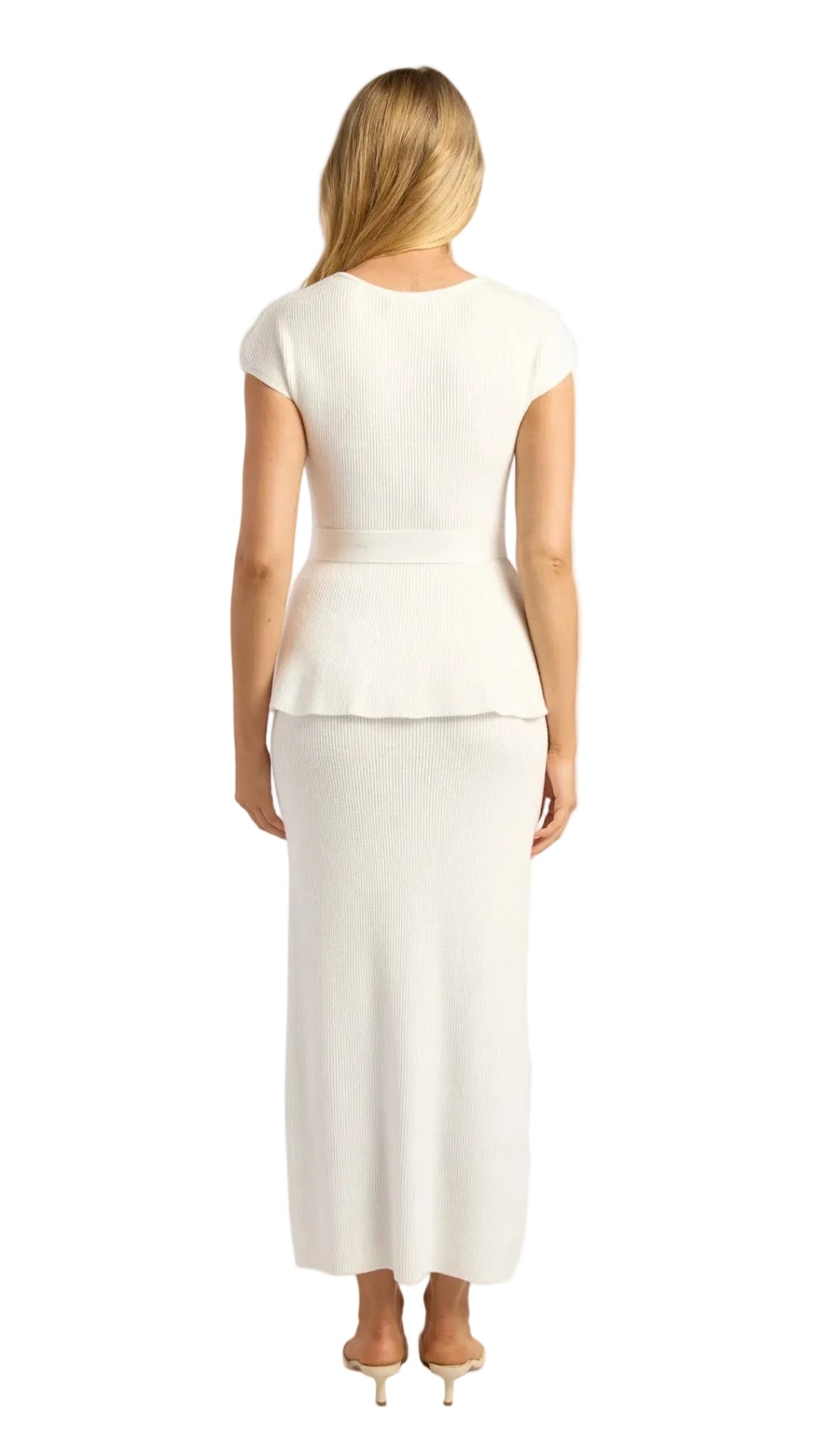 A woman viewed from the back wearing a white peplum top and matching midi skirt, paired with beige high-heeled sandals, against a light gray studio background.