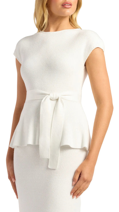A woman wearing a white ribbed knit peplum top with cap sleeves and a matching tie belt, paired with a white ribbed knit skirt against a light gray studio background.