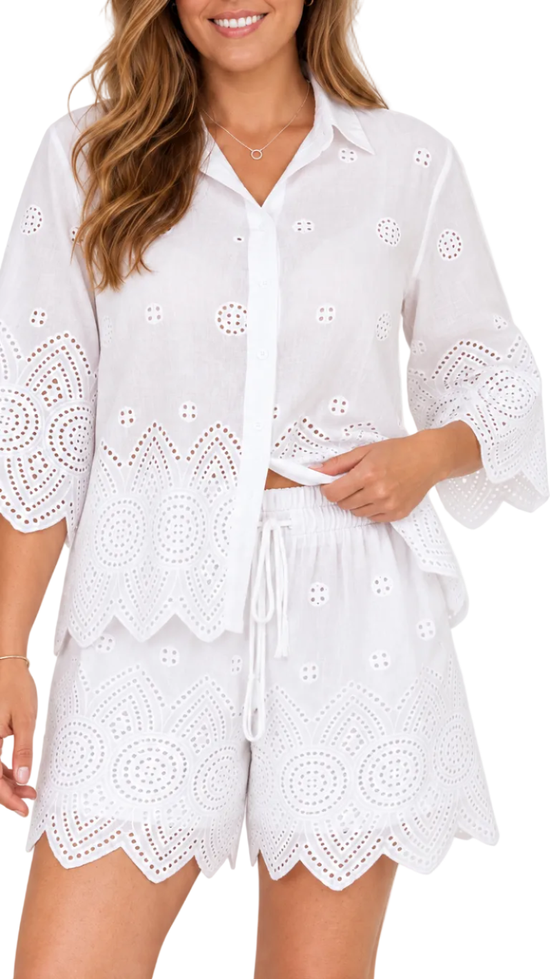 A woman wearing a white eyelet two-piece set consisting of a button-up shirt and matching shorts with a drawstring waist, photographed against a plain light background.
