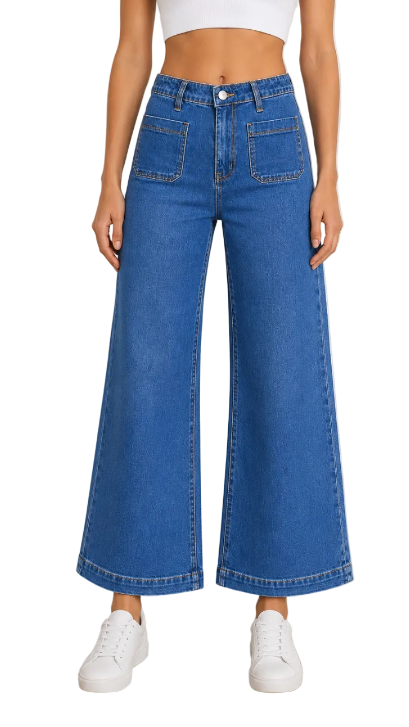 A model wearing a pair of high-waisted, wide-leg blue denim jeans with a white crop top and white sneakers, standing against a neutral studio background.