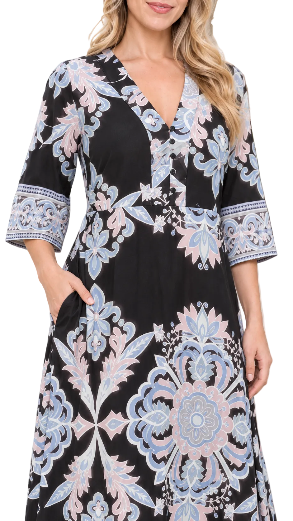 A woman wearing a black V-neck dress with a light blue and pale pink floral mandala pattern, featuring 3/4 sleeves with embroidered cuffs, set against a blurred outdoor background.