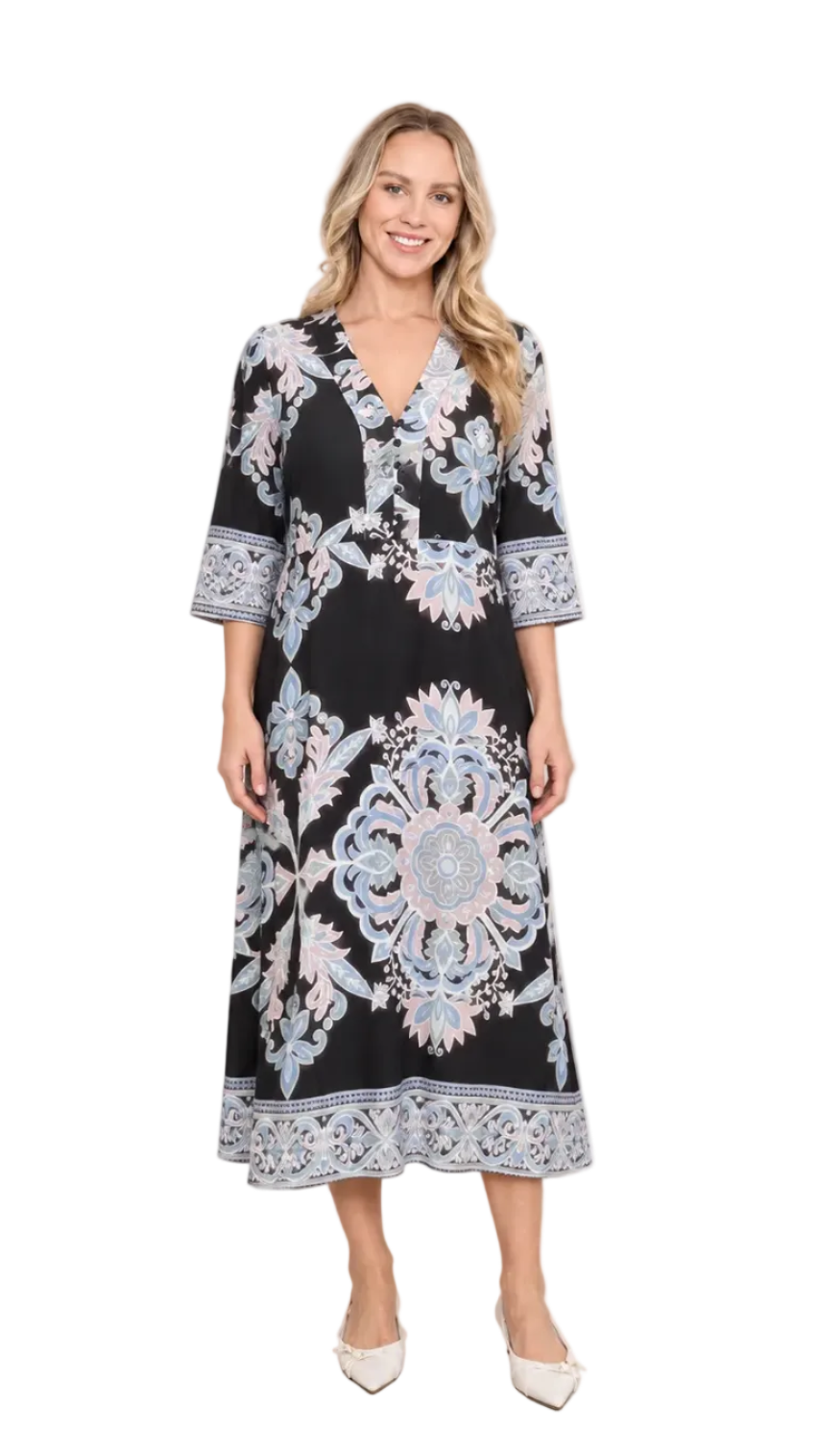 A woman modeling a black midi dress with a light blue and white floral mandala pattern, standing against a neutral beige textured backdrop.