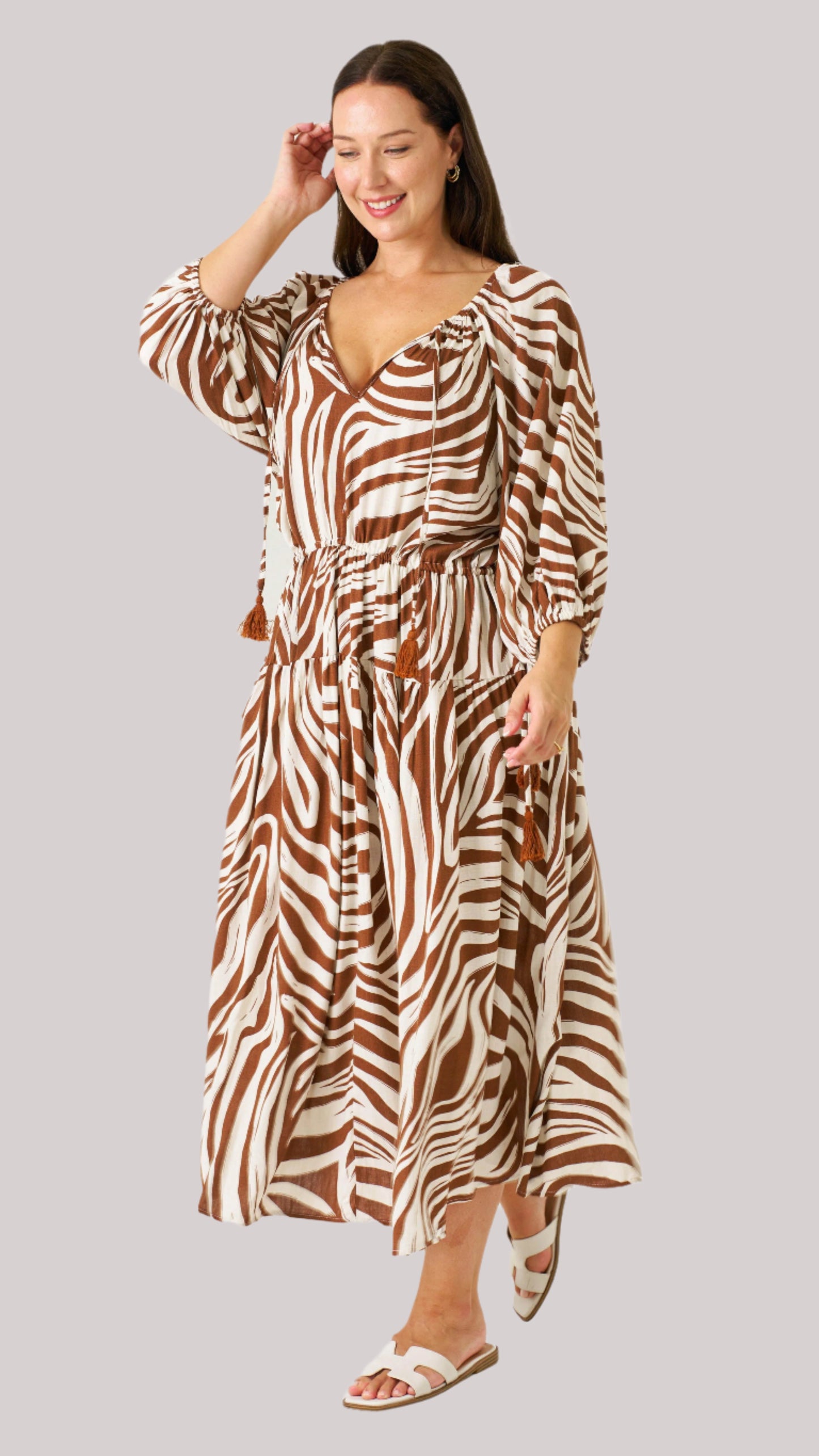 Model wearing the Zeeba Midi Dress in chocolate, smiling with hand in hair – full-length front view.