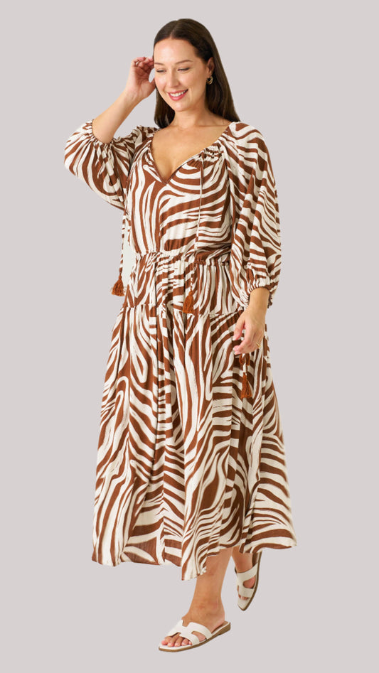 Model wearing the Zeeba Midi Dress in chocolate, smiling with hand in hair – full-length front view.
