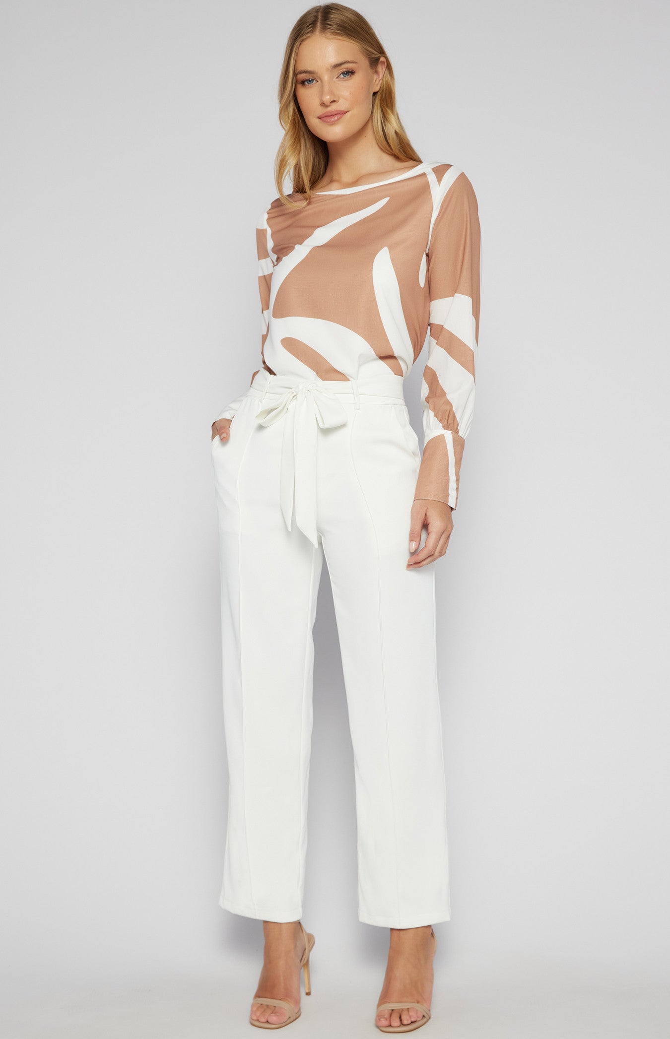 Woman wearing a sheer top and white pants on a plain background